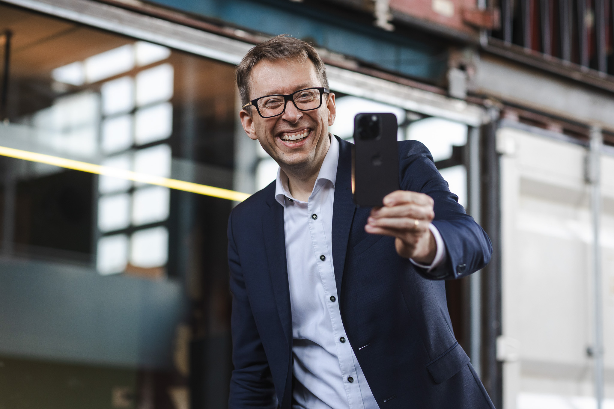 Daniel Schwenger lacht in die Kamera und hält ein Smartphone für ein Selfie hoch